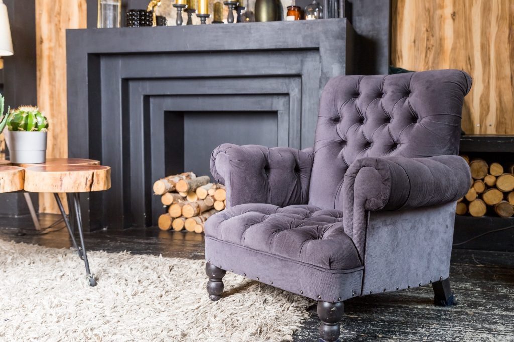 Elegant interior, dark armchair next to wooden table and faux fireplace.Cozy living room